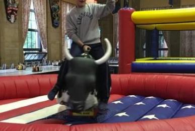 A student rides a mechanical bull.